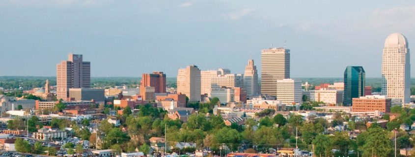 An arial view of downtown Winston-Salem features many tall buildings, highways, and parking lots.